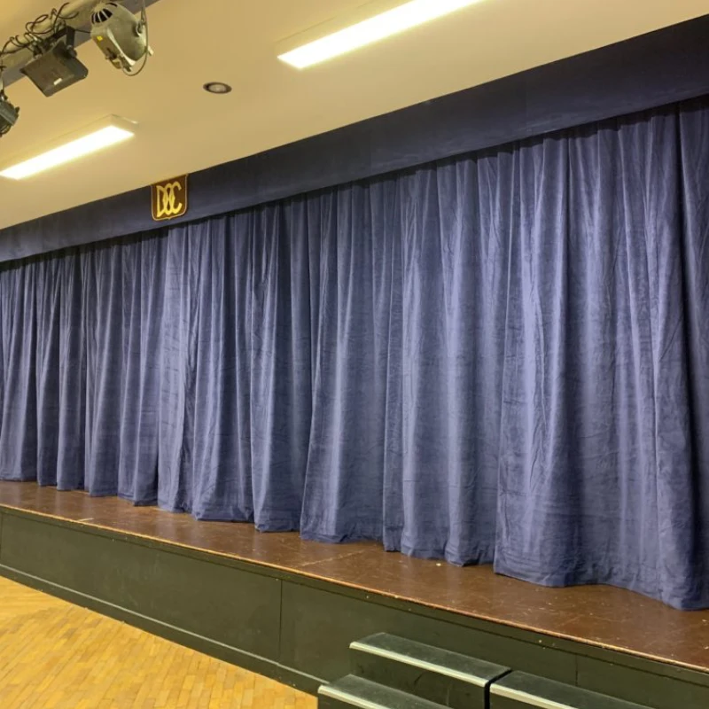 A stage with blue acoustic curtains and colorful lighting effects on the floor.