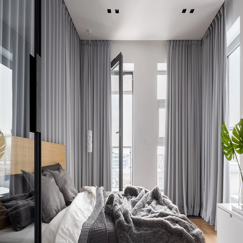 Modern bedroom with gray floor-to-ceiling curtains, a bed with gray bedding, and a large plant.