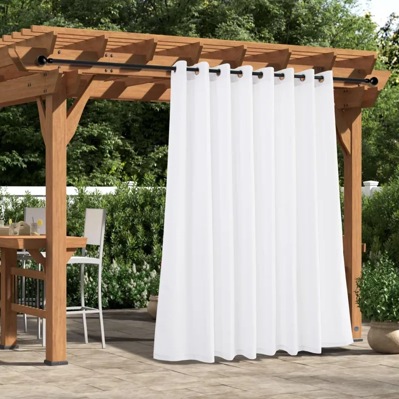 White outdoor curtains hang from a wooden pergola.