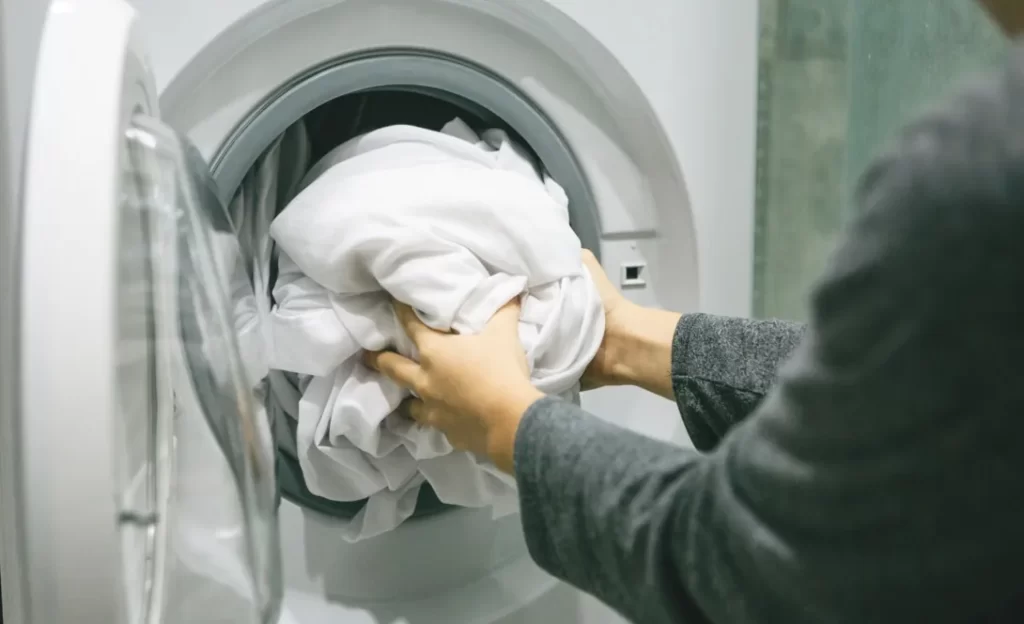 The person loads white laundry into a front-loading washing machine.