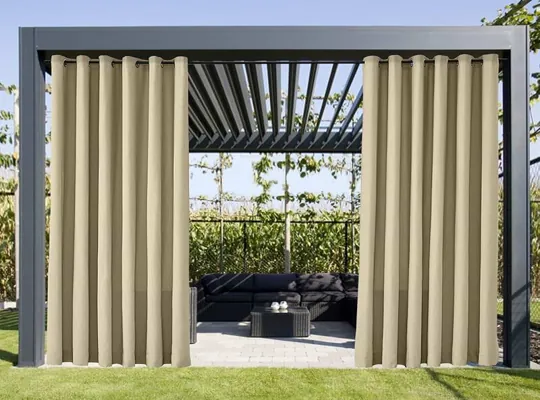 Outdoor patio pergola with open light-colored privacy curtains revealing a seating area, surrounded by greenery.